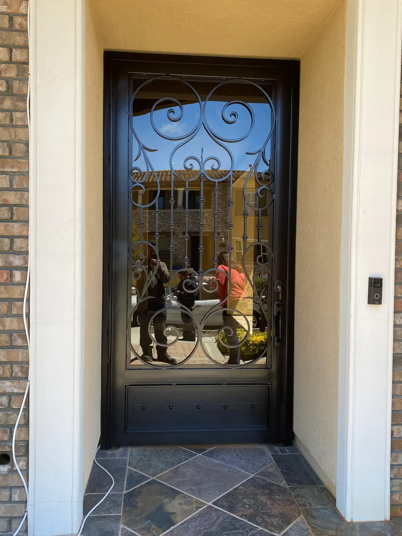 Black ornamental security door with symmetrical scrollwork and a solid lower panel